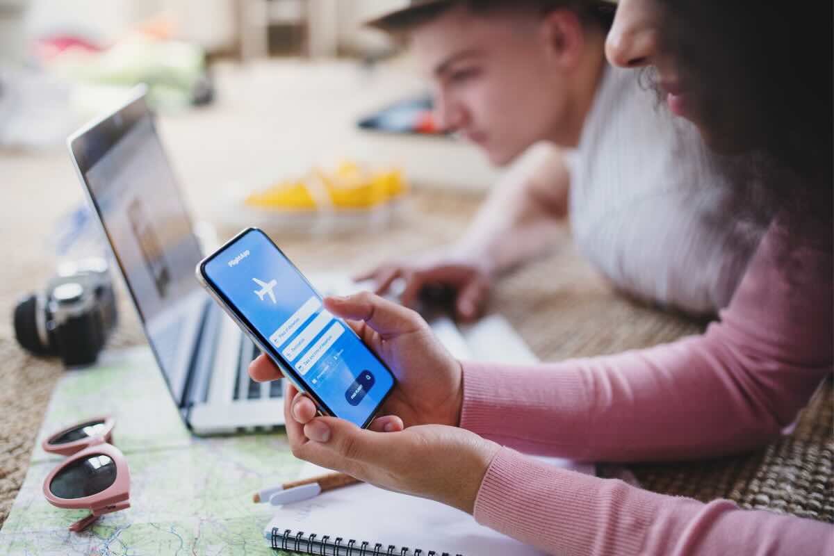 ragazzo e ragazza con pc e smartphone che prenotano vacanze